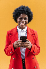 African American woman looking at the camera and laughing while holding a mobile phone. Technology concept.