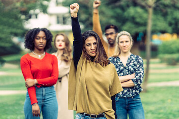 woman with latin features raises her fist protesting inequality between men and women with 4 people behind her 