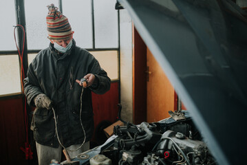 Old man with protective mask in the garage repair his old car.