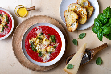 Homemade Italian tomato or roasted pepper soup with tortellini, pesto and parmesan cheese. Top view
