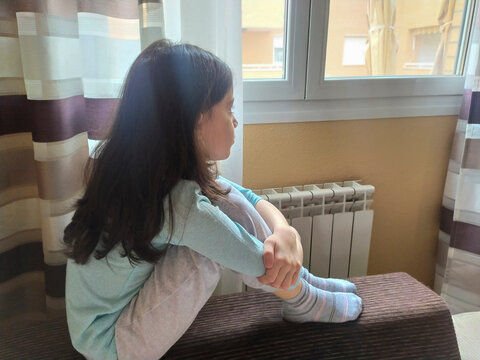 Girl sitting looking out the window of her house