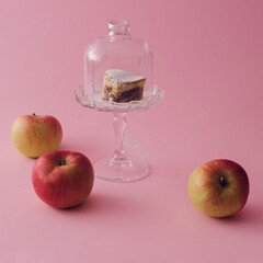 Delicious heart-shaped apple cakes sprinkled with powdered sugar on a beautiful glass plate in the middle of the composition.  Beautiful ripe apples scattered around on a pastel pink background