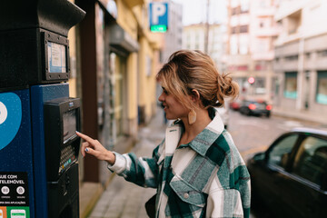 Photo of charming young pretty girl with collected hair wearing bright shirt using parking meter for parking her auto. Traveling concept 
