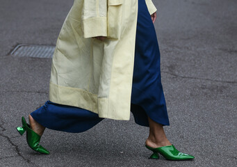 woman wearing blue pants, light yellow coat and forest green shoes