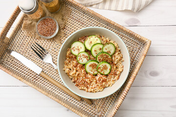 Bowl with tasty oatmeal, flax seeds and cucumber on tray