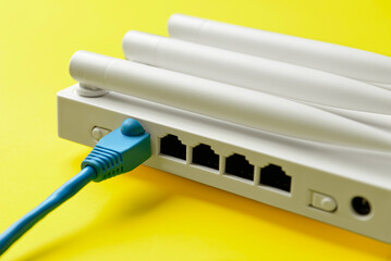 Wi-Fi router with antennas and network cable on color background