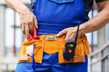Fototapeta na wymiar Male worker with tool belt and radio transmitter at construction site