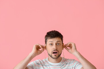 Shocked handsome man with ear plugs on pink background
