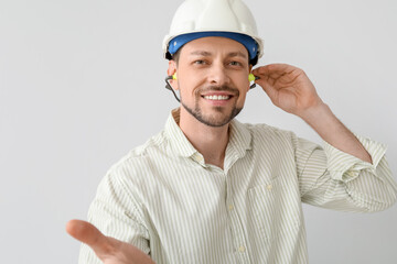 Handsome man in hardhat with ear plugs on light background