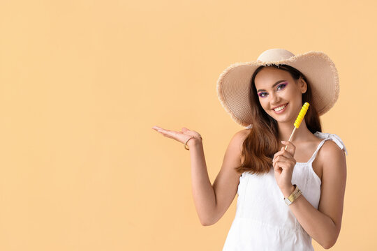Beautiful young woman in hat with sweet lollipop on beige background