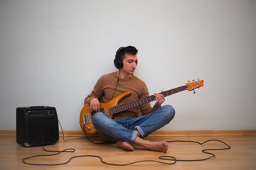 Young man playing on a guitar with wall on the background