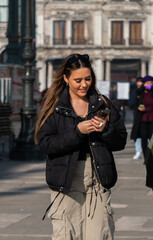 Fototapeta premium woman walking in the city, wearing sunglasses and a stylish outfit. she is wearing sunglasses on her head and looking at her phone