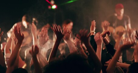 The band that brought everyone together. Group of young, fun loving people celebrating and dancing under strobe lights. Crowd cheering with hands raised at a festival, concert, party, or rave