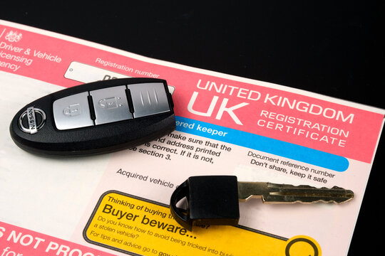 Genuine UK registration certificate for a purchased car and car key on top of it. Registration document also known as a vehicle log book V5C. Stafford, United Kingdom, January 30, 2022.