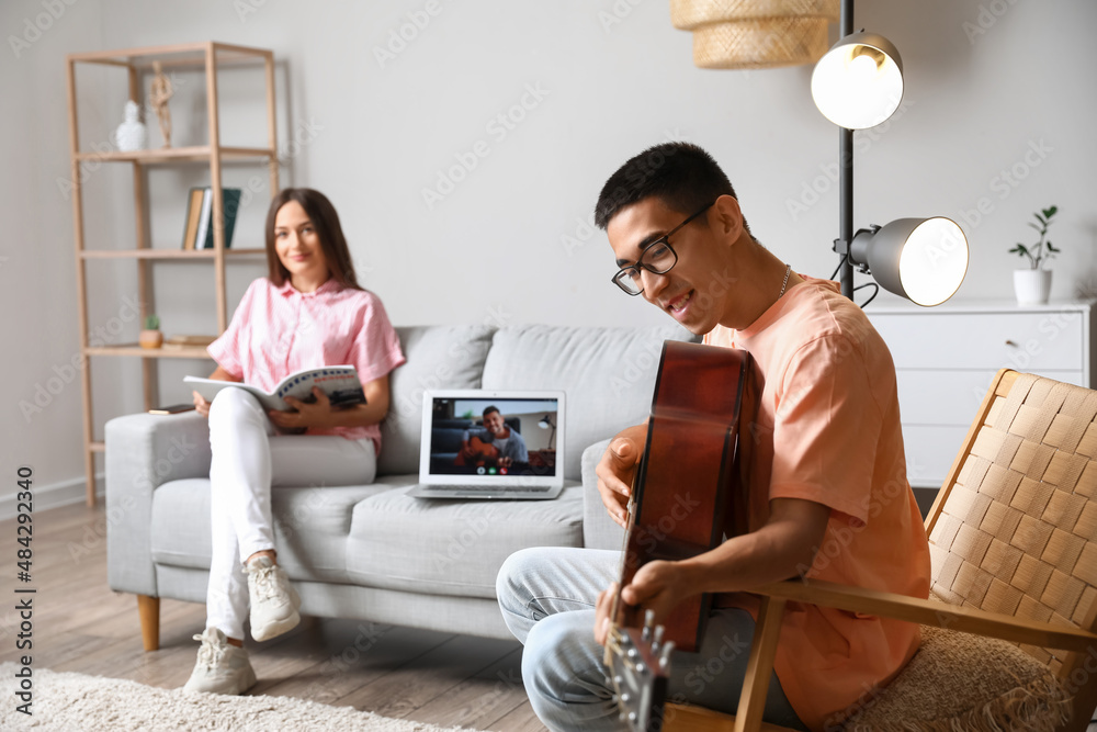 Poster young man having online guitar lesson at home