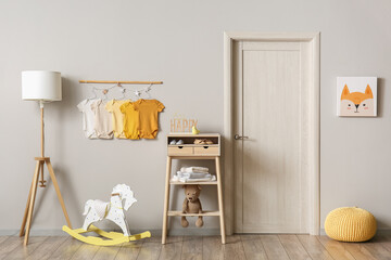 Interior of light children's room with baby bodysuits, lamp and table