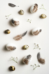 Happy Easter flat lay composition. Easter eggs decorated feathers with gypsophila flowers on white background. Elegant, minimal style.