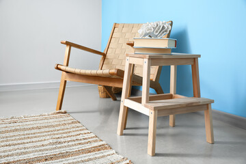 Wooden step stool with decor, books and armchair near blue wall