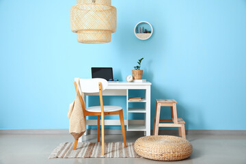 Fototapeta na wymiar Modern workplace with laptop, pouf and wooden step stool near blue wall