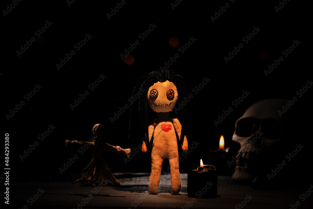 Wall mural Female voodoo doll with pin in heart and ceremonial items on table in darkness