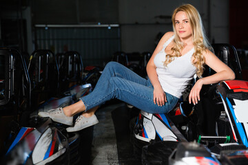 Fototapeta na wymiar Young glad positive smiling woman with helmet sitting in car for karting in sport club