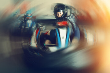Young woman in helmet and other people driving go-kart cars in sport club indoor