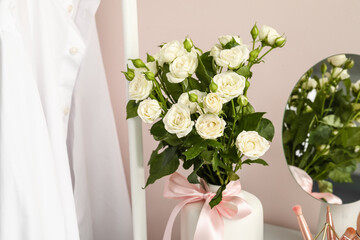 Vase with bouquet of beautiful roses near light wall