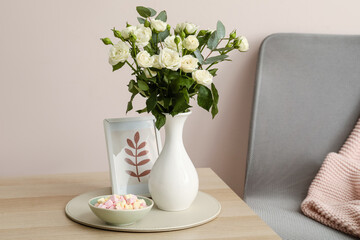 Vase with bouquet of beautiful roses and marshmallows on table in room