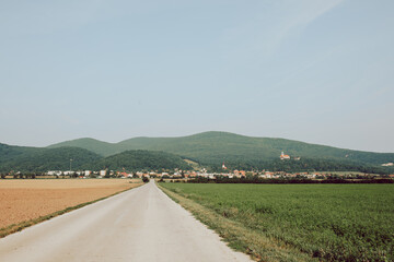 Road and fields with hills and village in the background taken on sunny summer day
