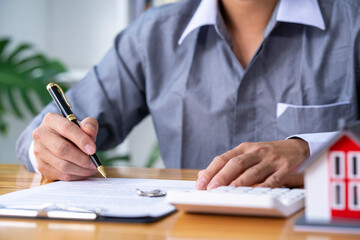 Real estate agent working sign agreement document contract for home loan insurance approving purchases for a client with house model and key on the table, concept of a contract to buy and sell a house
