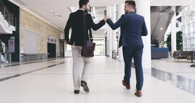 Venture together and start this adventure. Businessmen giving each other a fist bump while walking in a convention centre or office. Diverse colleagues greeting and talking for teamwork and unity