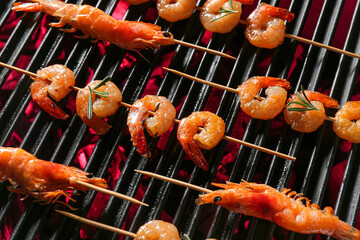 Wooden skewers with delicious shrimps on grill, closeup