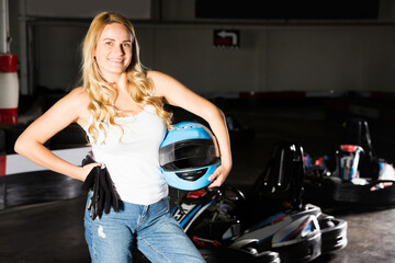 Fototapeta na wymiar Cheerful blonde smiling girl posing with helmet in her hands at kart circuit
