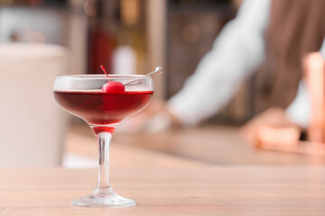 Glass of tasty Manhattan cocktail with cherry on table