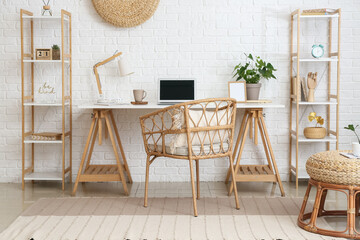 Workplace with modern laptop near white brick wall in light room interior