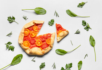 Tasty tomato galette and greens on light background