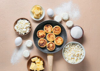 Frying pan with cottage cheese pancakes and ingredients on beige background