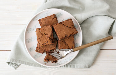 Plate with pieces of tasty chocolate brownie on white wooden background
