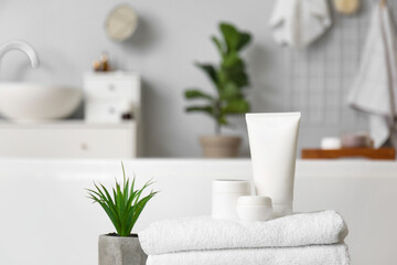 Set of cosmetic products, towels and plant in bathroom