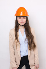 A girl architect in a suit and an orange construction helmet stands on a white background.