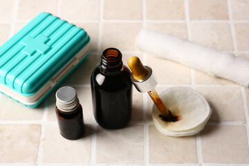 Bottles with iodine, pipette, cotton pads, first aid kit and gauze roll on tile background
