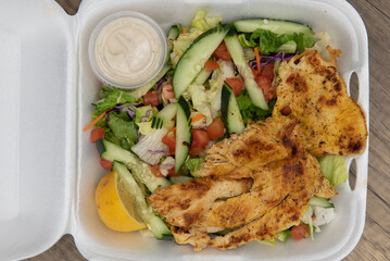 Overhead view of take out order of grilled chicken salad completely filling the styrofoam box
