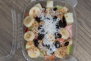 Overhead view of healthy take out order of sliced bananas, raisins, cocnut, nuts, and mango makes this plastic box full