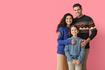 Little girl with her parents in warm sweaters hugging on pink background