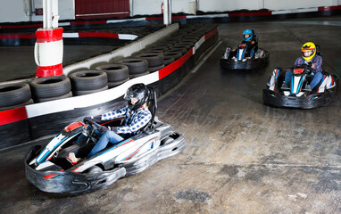 Glad people in helmets driving cars for karting in sport club indoor
