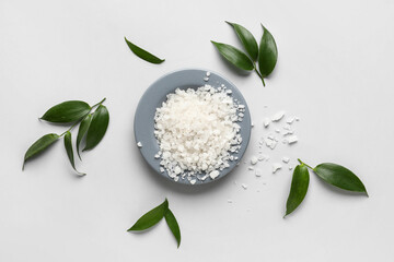 Bowl of sea salt and plant leaves on white background