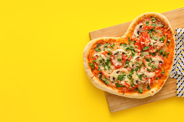 Wooden board with tasty heart-shaped pizza on yellow background. Valentine's Day celebration
