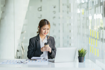 Beautiful asian lady working at modern office, drinking coffee.