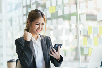 Emotional happy millennial asian woman looking at smartphone screen, reading message with unbelievable amazing news, celebrating getting online shopping prize or lottery win notification.