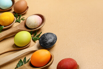 Spoons with painted Easter eggs on color background
